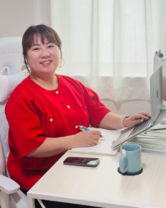 主催の戸井田桃子。赤い服でパソコンと手帳を広げ、机に向かってほほえんでいるプロフィール写真